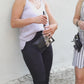 A person with a  black vegan leather phone pouch with a black vegan leather magnetic wristlet key chain and a black removable three pocket wallet and black lip balm holder set. Another Person  with a black and gray vegan leather bracelet, keychain, three pocket wallet, and a black lip balm holder used as a fanny pack belt bag. 
